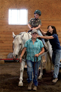 Therapist Vera Liljistrand, MS-SLP and patient Wade West share a moment as Wade repeats target speech sounds during his speech therapy session on Dooleys Blue Lake. Casey West provides the horse handling for “Dooley,” a former team roping horse. (Credit: Andrea Caudill)